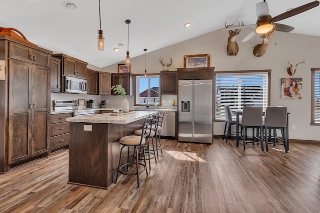 kitchen with wood finished floors, light countertops, appliances with stainless steel finishes, a kitchen breakfast bar, and a center island