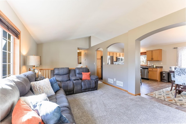 living area featuring arched walkways, visible vents, plenty of natural light, and vaulted ceiling