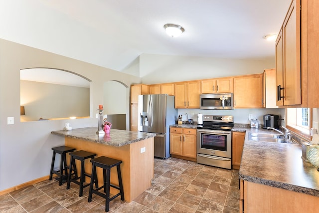 kitchen with dark countertops, a breakfast bar area, lofted ceiling, appliances with stainless steel finishes, and a sink