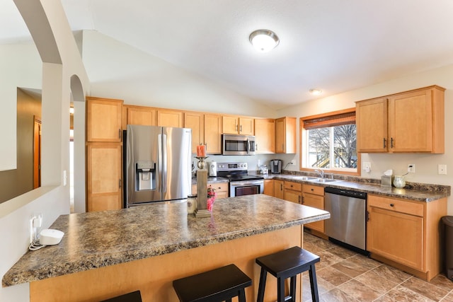 kitchen featuring lofted ceiling, a peninsula, appliances with stainless steel finishes, dark countertops, and a kitchen breakfast bar