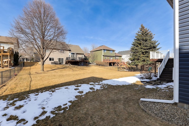 yard layered in snow featuring a wooden deck, a residential view, stairway, and fence