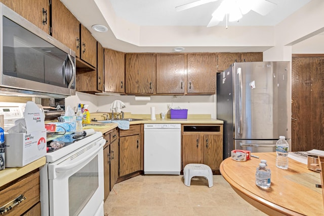 kitchen with a ceiling fan, a sink, stainless steel appliances, light countertops, and brown cabinets