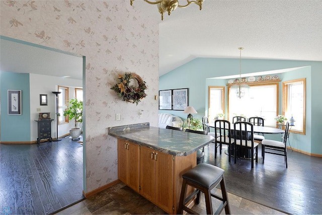 kitchen with dark countertops, wallpapered walls, vaulted ceiling, brown cabinets, and a peninsula