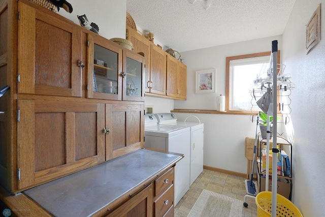 clothes washing area with cabinet space, washer and dryer, a textured ceiling, and baseboards