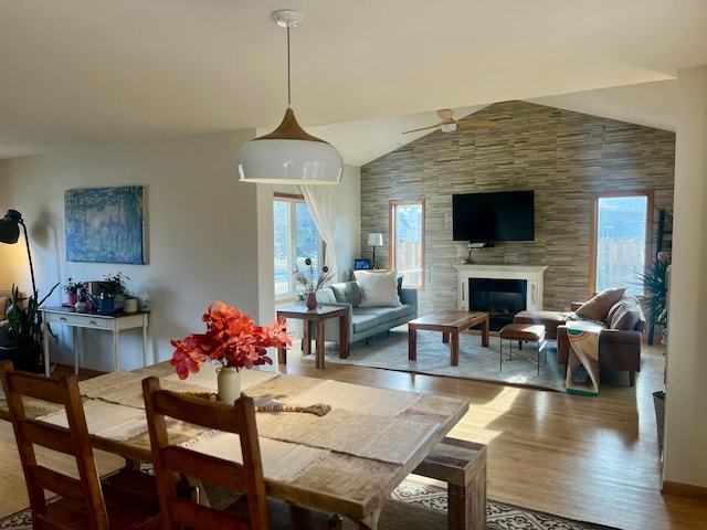 dining space with wood finished floors, lofted ceiling, a glass covered fireplace, and a ceiling fan