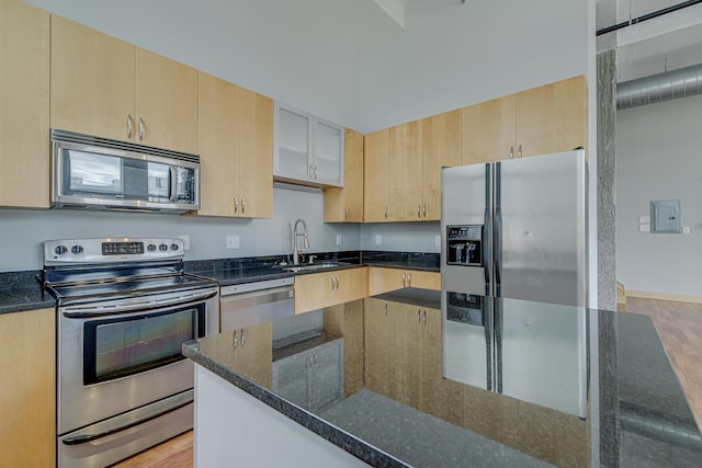 kitchen with light brown cabinetry, a sink, electric panel, dark stone countertops, and stainless steel appliances