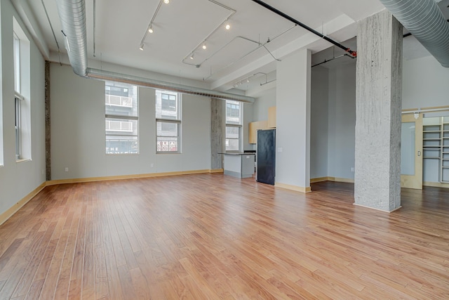 unfurnished living room featuring light wood-style flooring, baseboards, and a towering ceiling