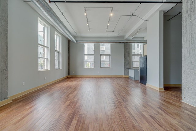 unfurnished living room featuring baseboards, plenty of natural light, wood finished floors, and rail lighting