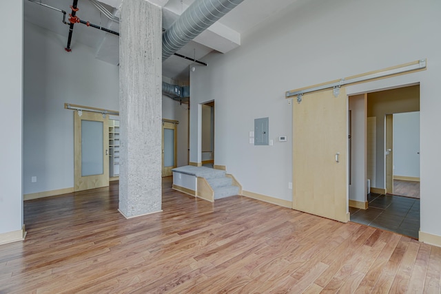 unfurnished living room featuring electric panel, a high ceiling, a barn door, and wood finished floors