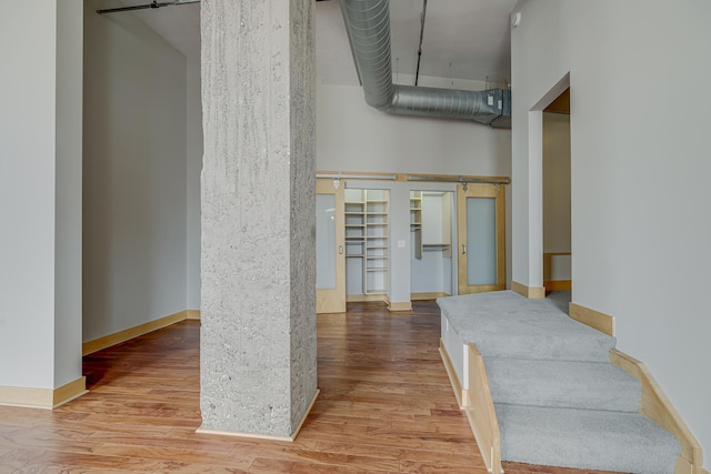 hall featuring a towering ceiling, a barn door, and wood finished floors