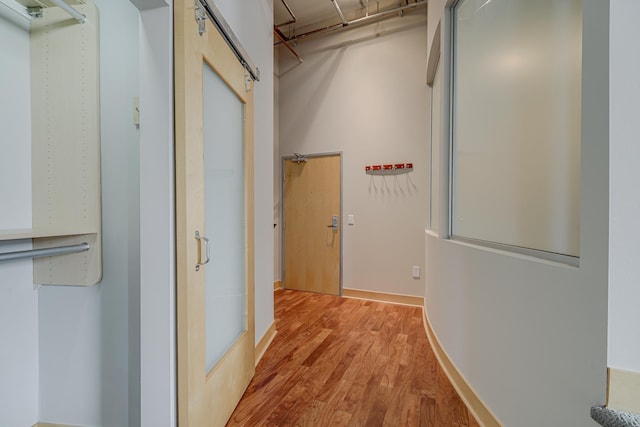 corridor featuring light wood-type flooring, a barn door, and baseboards