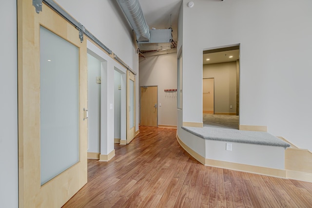 corridor featuring a barn door, a high ceiling, baseboards, and light wood finished floors