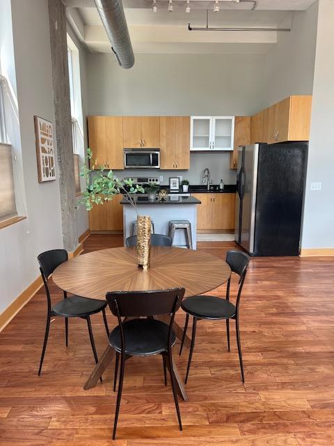 kitchen with light brown cabinets, a high ceiling, light wood-style floors, stainless steel appliances, and a sink