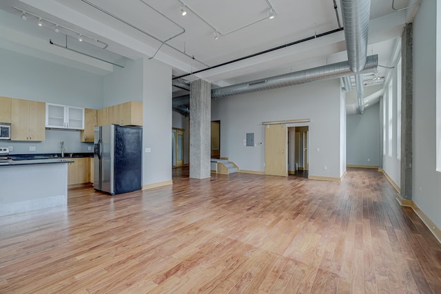 unfurnished living room featuring track lighting, a sink, light wood finished floors, baseboards, and a towering ceiling