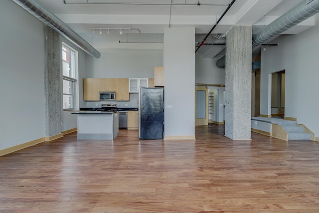 kitchen featuring stainless steel appliances, open floor plan, dark countertops, and a towering ceiling