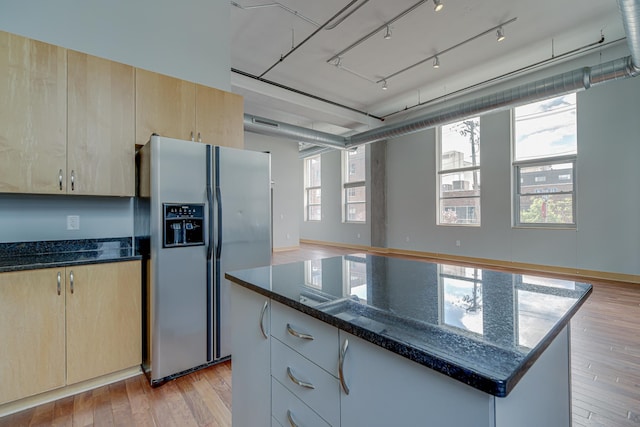 kitchen with light brown cabinets, light wood-style floors, stainless steel fridge with ice dispenser, and dark stone counters