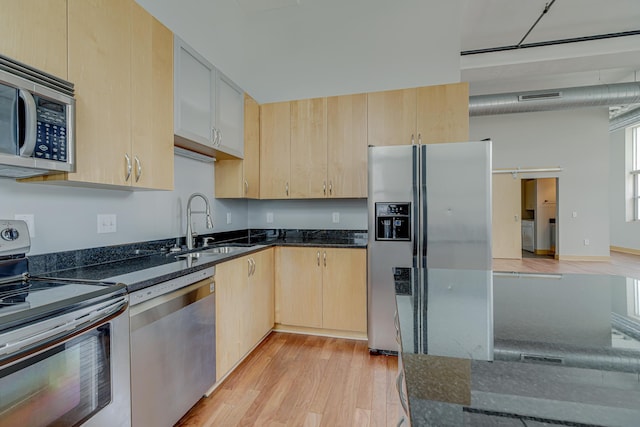 kitchen featuring dark stone countertops, a sink, light brown cabinetry, light wood-style floors, and appliances with stainless steel finishes