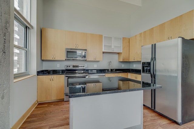 kitchen featuring a towering ceiling, light wood-type flooring, light brown cabinetry, and stainless steel appliances