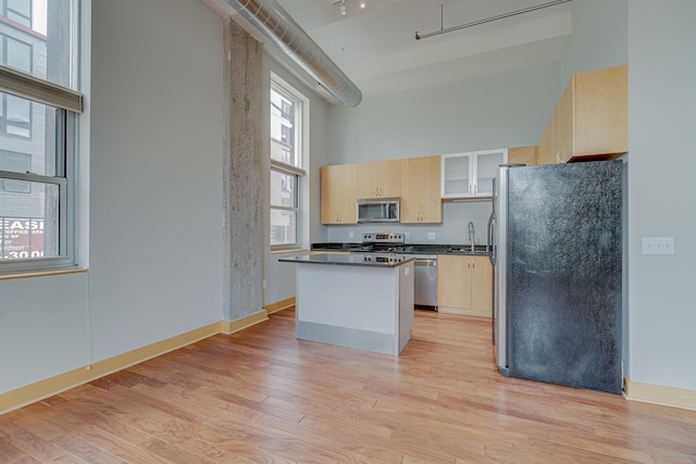 kitchen featuring light brown cabinetry, a sink, a center island, appliances with stainless steel finishes, and a towering ceiling