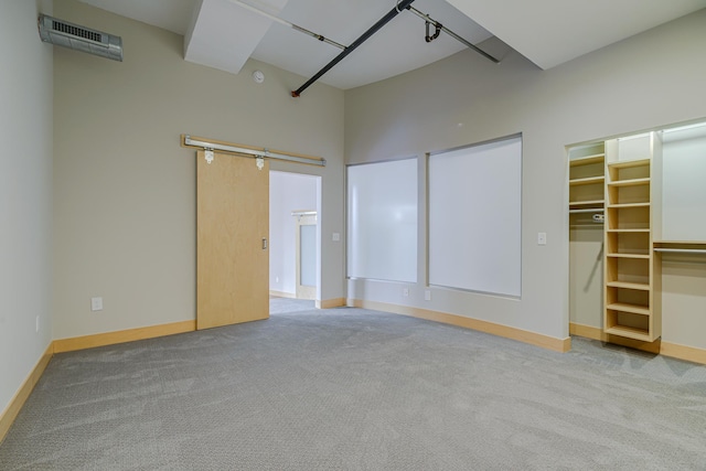 unfurnished bedroom with visible vents, a walk in closet, a barn door, carpet, and baseboards