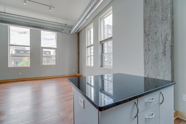 kitchen with dark stone countertops, rail lighting, baseboards, and light wood-type flooring