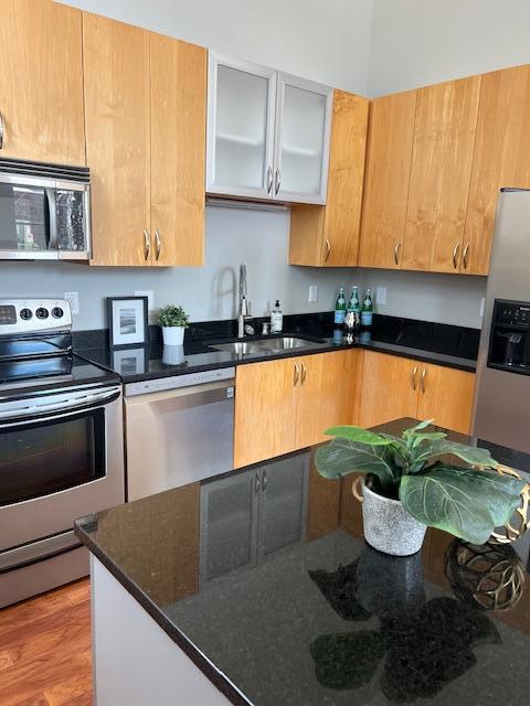 kitchen with a sink, dark stone countertops, light wood-style floors, appliances with stainless steel finishes, and glass insert cabinets