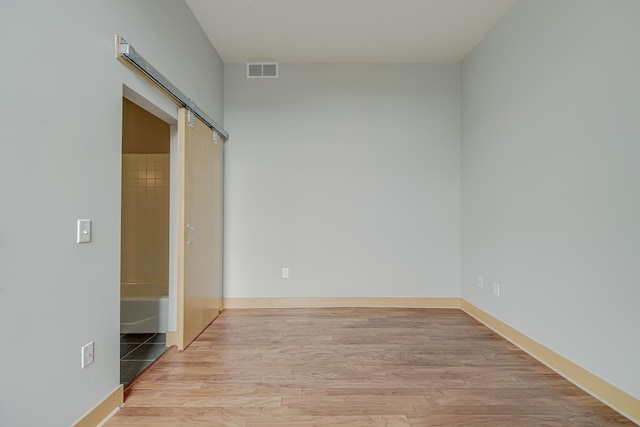 unfurnished room featuring a barn door, wood finished floors, visible vents, and baseboards