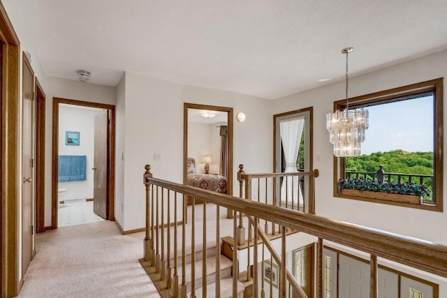 corridor with a notable chandelier, an upstairs landing, baseboards, and light carpet