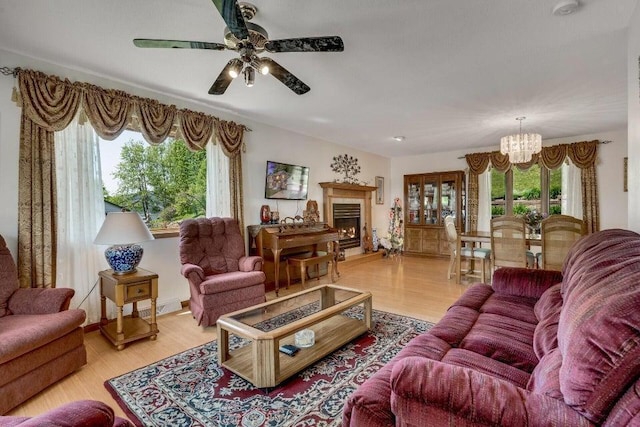 living room featuring visible vents, a lit fireplace, wood finished floors, and ceiling fan with notable chandelier