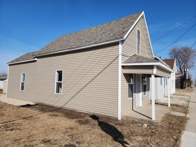 view of side of home with a patio and roof with shingles