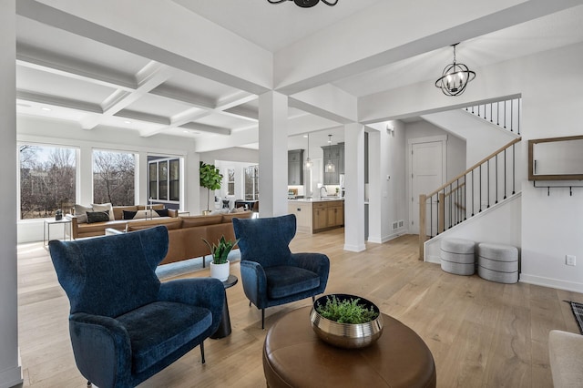 living area featuring beam ceiling, coffered ceiling, light wood-style floors, baseboards, and a chandelier