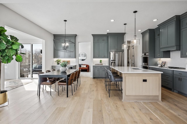 kitchen featuring a sink, backsplash, light wood-style floors, appliances with stainless steel finishes, and a chandelier