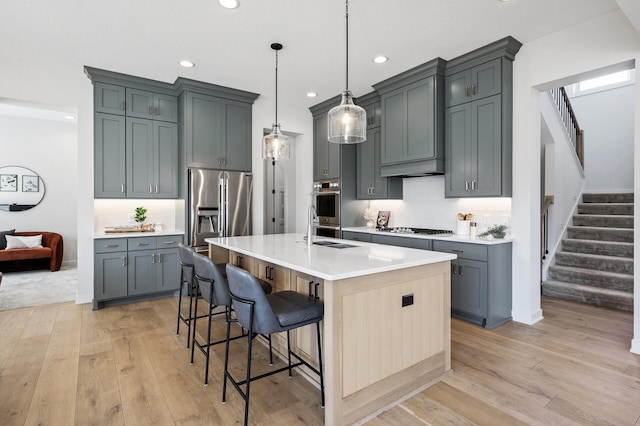 kitchen featuring a breakfast bar, a sink, light countertops, appliances with stainless steel finishes, and light wood-type flooring