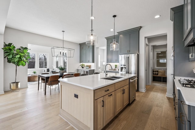 kitchen with a sink, light wood-type flooring, light countertops, stainless steel appliances, and a kitchen island with sink