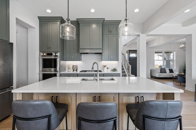 kitchen featuring a breakfast bar, a sink, backsplash, appliances with stainless steel finishes, and light wood finished floors