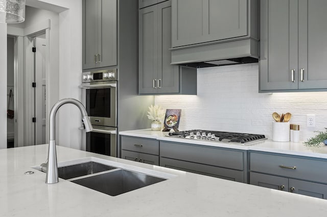 kitchen with premium range hood, gray cabinets, a sink, tasteful backsplash, and stainless steel appliances