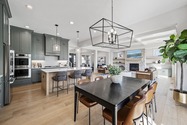 dining room with light wood-type flooring, recessed lighting, a fireplace, an inviting chandelier, and coffered ceiling