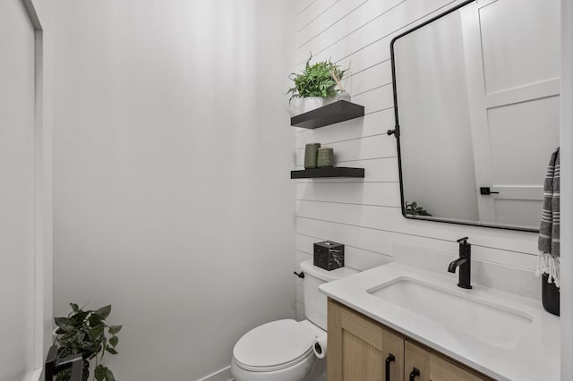 bathroom featuring wooden walls, toilet, and vanity