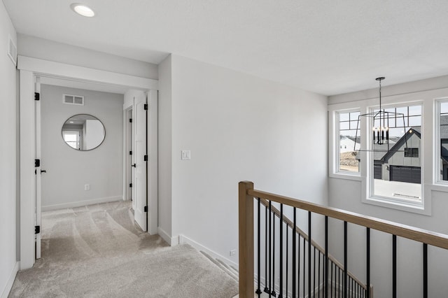 hall featuring visible vents, baseboards, a chandelier, light colored carpet, and an upstairs landing