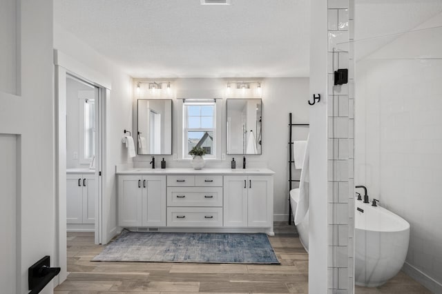 bathroom with double vanity, a textured ceiling, a freestanding bath, and wood finished floors