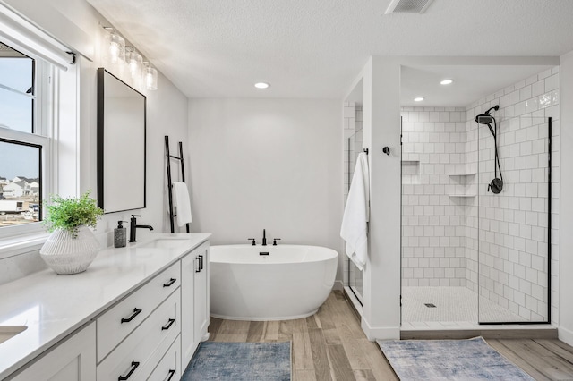 full bath featuring a shower stall, a freestanding bath, wood finished floors, and a sink