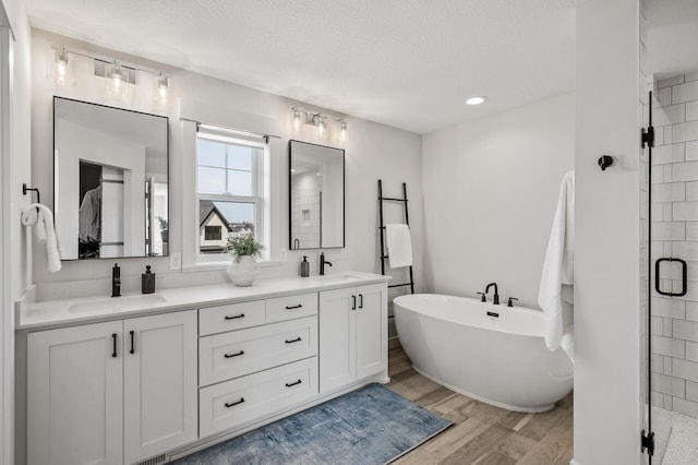 bathroom with a sink, a textured ceiling, wood finished floors, a shower stall, and a freestanding bath