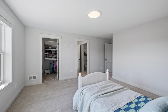 bedroom with light carpet, visible vents, a walk in closet, and baseboards