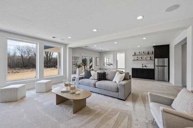 living room featuring light carpet, a textured ceiling, recessed lighting, indoor wet bar, and baseboards