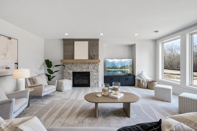 carpeted living room with recessed lighting, a textured ceiling, and a stone fireplace