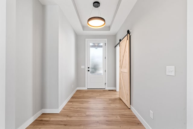 doorway to outside with baseboards, light wood-type flooring, a tray ceiling, and a barn door