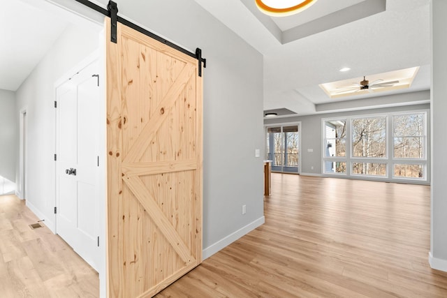 hall featuring recessed lighting, a barn door, baseboards, light wood-style floors, and a raised ceiling