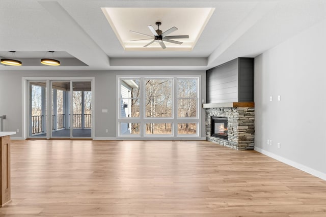 unfurnished living room with light wood finished floors, plenty of natural light, a fireplace, and a raised ceiling