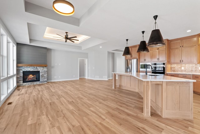 kitchen featuring light wood finished floors, stainless steel appliances, decorative backsplash, light countertops, and a raised ceiling