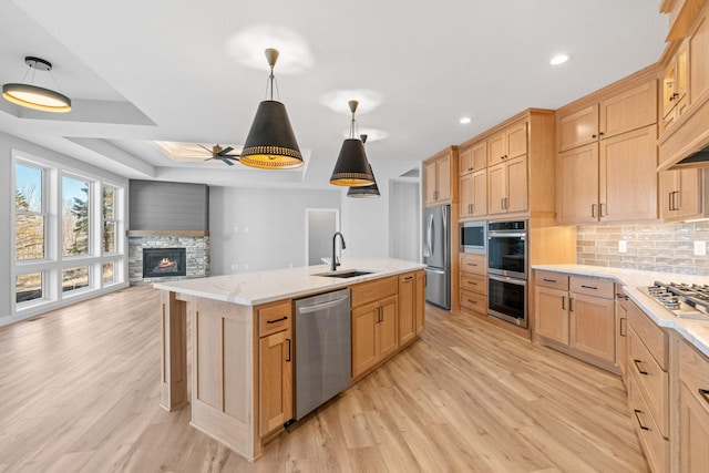 kitchen featuring light brown cabinetry, a sink, backsplash, open floor plan, and appliances with stainless steel finishes